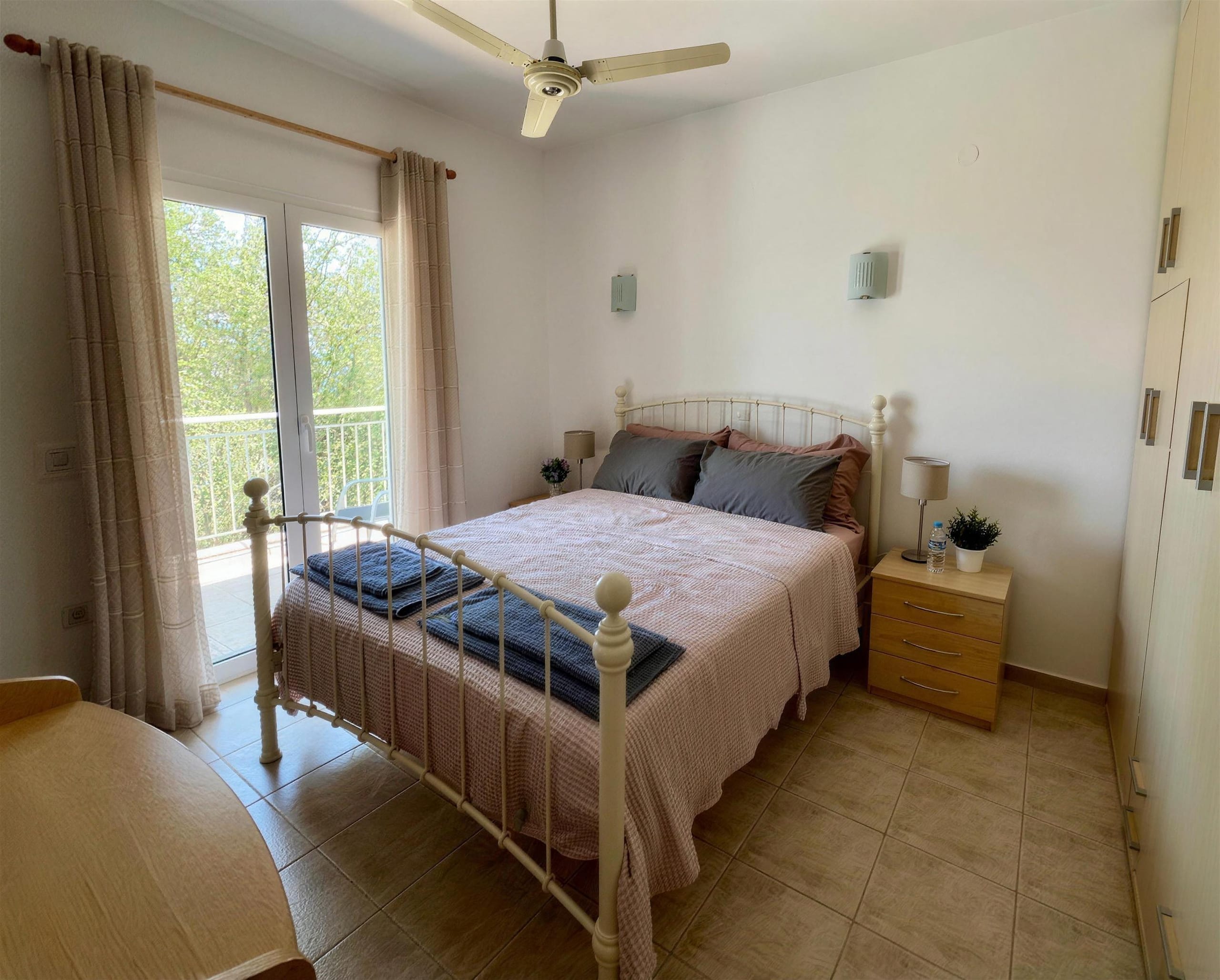 A double bedroom with an iron bedstead, a ceiling fan and doors to the balcony