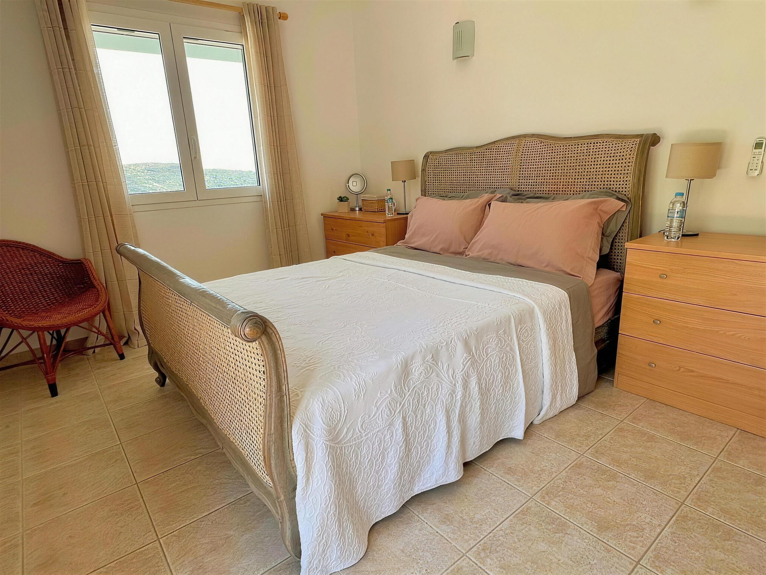 A bedroom with a rattan bedstead, a chest of drawers and a window over the bay