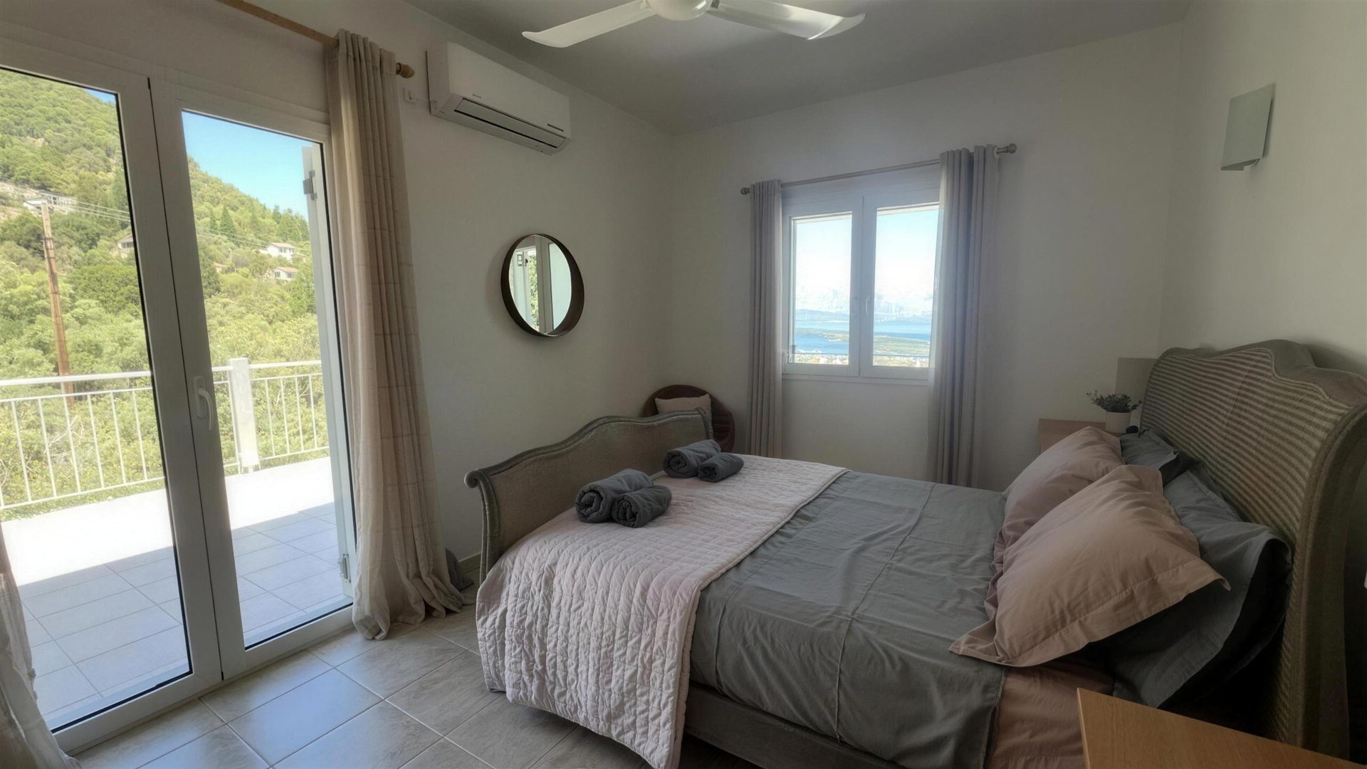 A double bedroom with its balcony doors open onto the trees and the sea