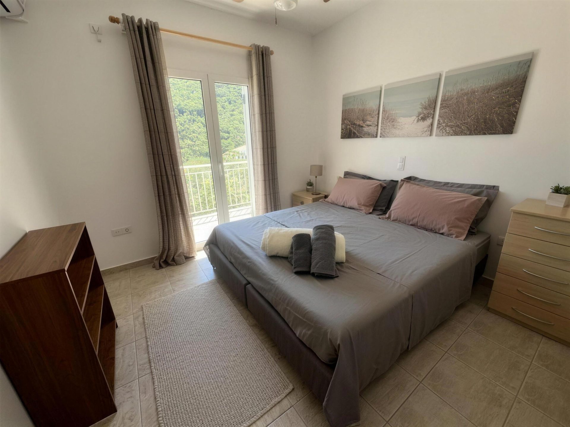 A double bed in grey linen under a pair of framed prints, doors to the garden