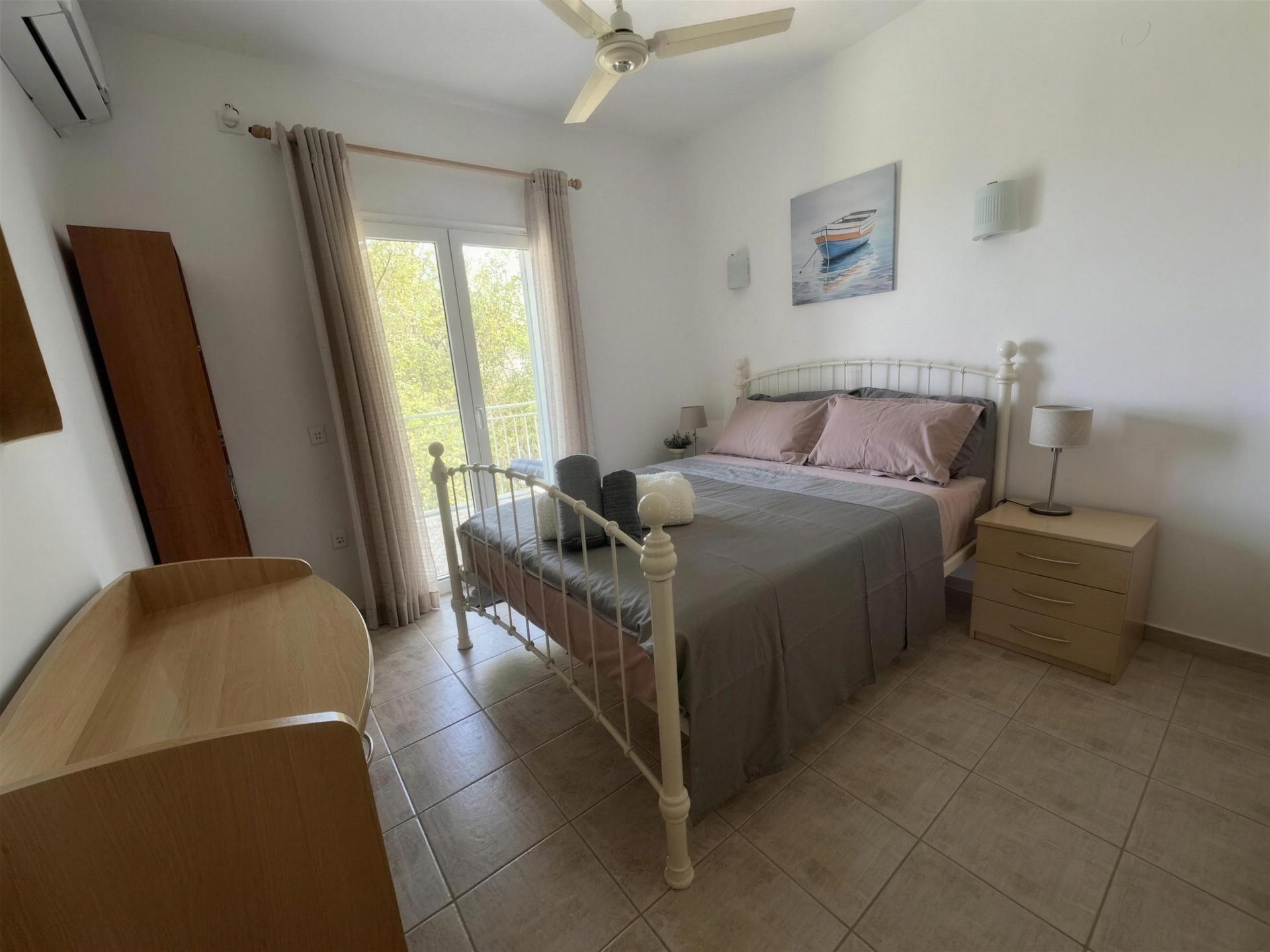 A bed with a black iron bedstead, ceiling fan above and a window onto the garden