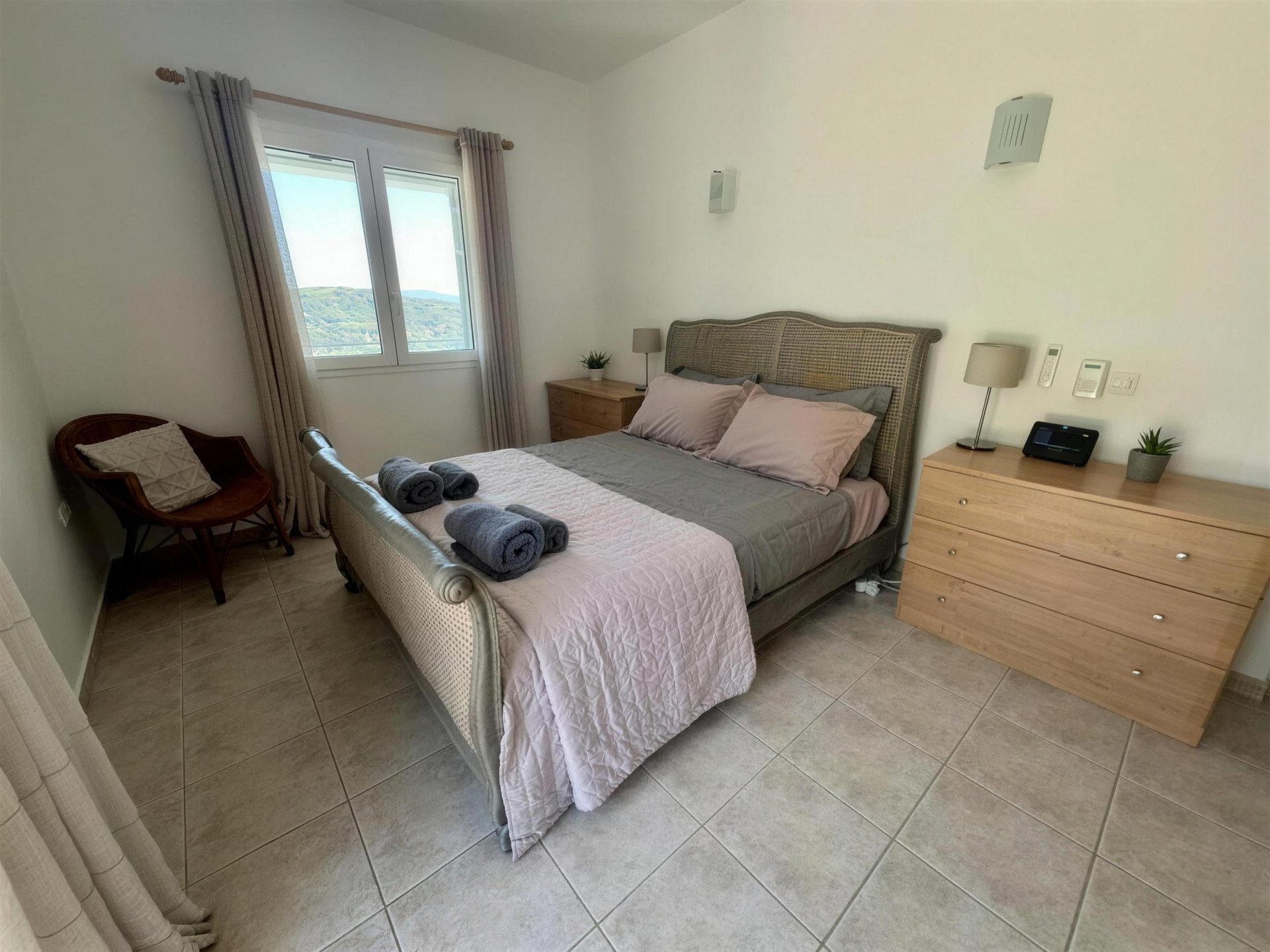 A double bed made up in white and rose, a window to the hillside beyond