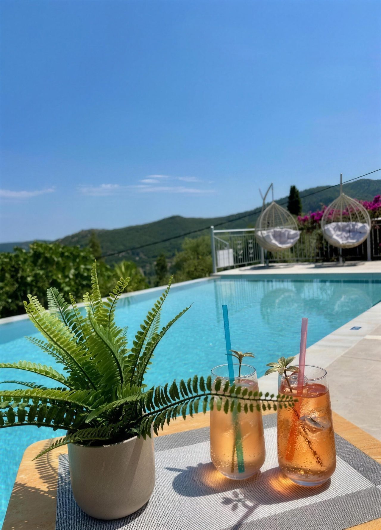 Two iced drinks on a table beside the pool, the bay behind