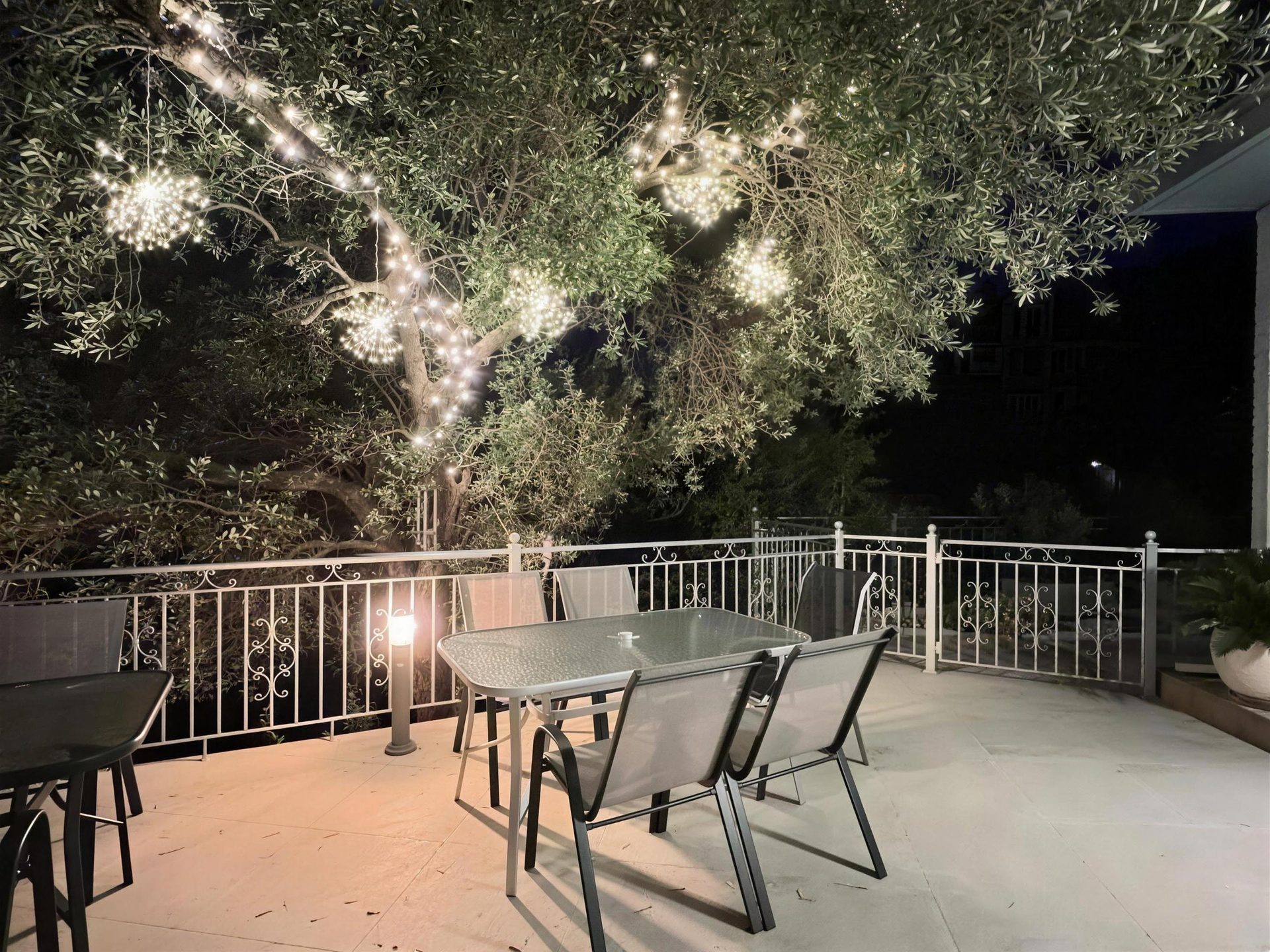 Festoon lights through the olive tree over the terrace table after dark