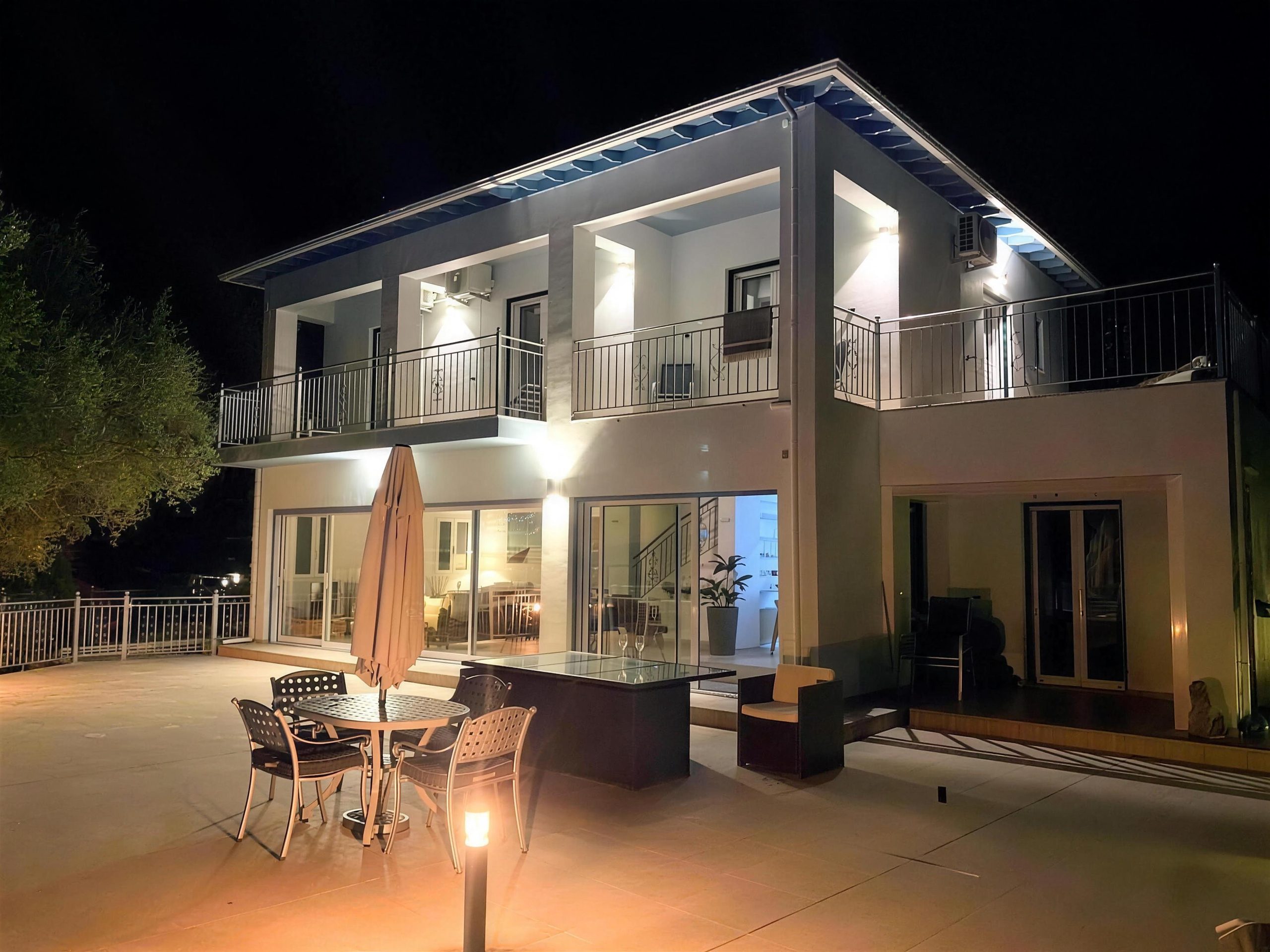 The villa lit after dark, the terrace table set below it