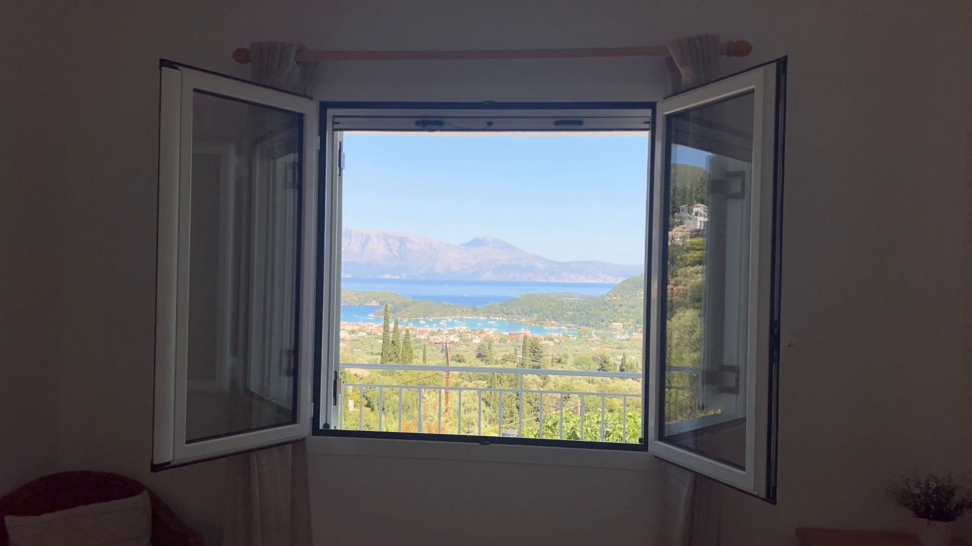 A bedroom window standing open on Nidri Bay, the harbour and the mainland mountains